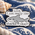 Shark quote enamel pin on navy ocean-patterned canvas with a seashell