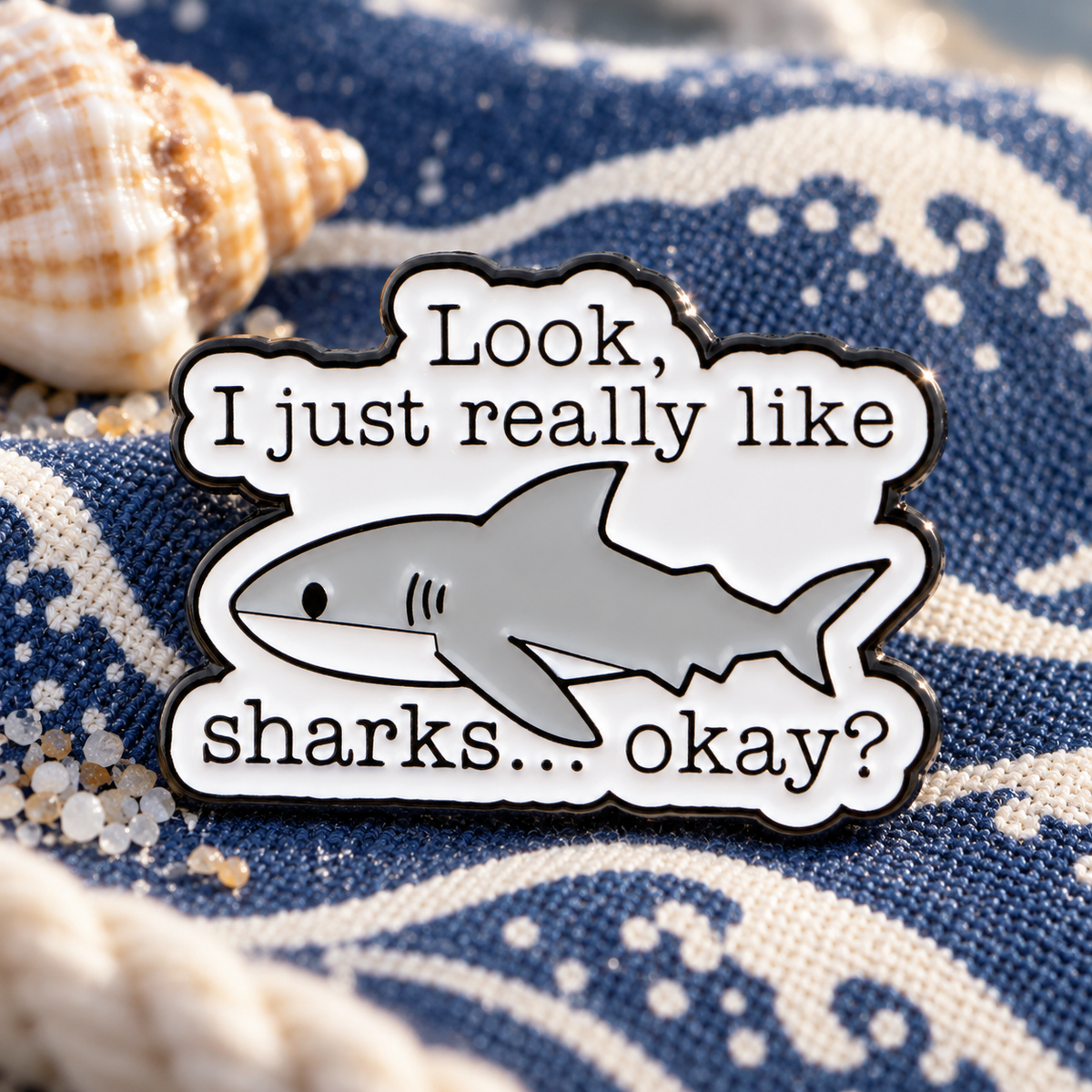 Shark quote enamel pin on navy ocean-patterned canvas with a seashell