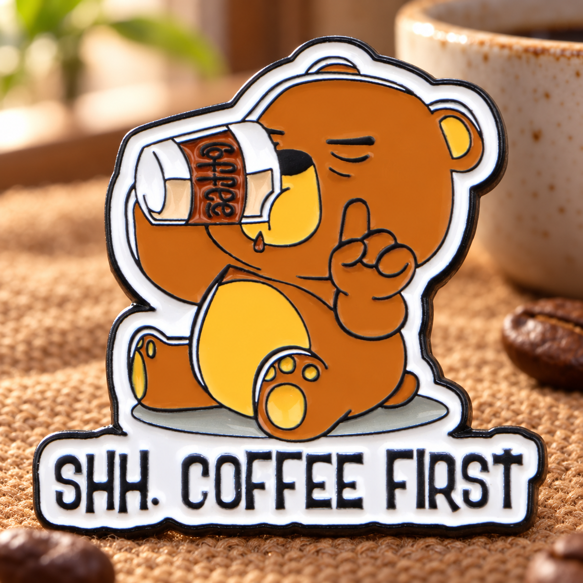 Shh. Coffee First Bear enamel pin on warm coffee-shop fabric
