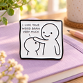 I Like Your Weird Brain enamel pin on a lavender notebook