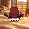 Tiny cat under an oversized cowboy hat enamel pin in a warm western setting