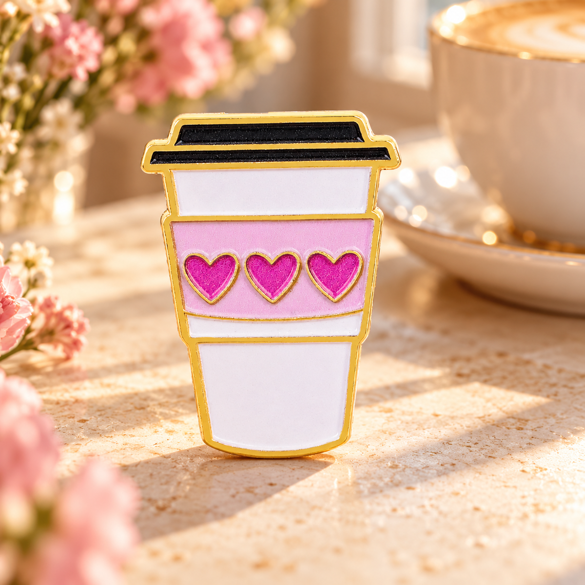 Pink heart coffee cup enamel pin in a warm sunlit café