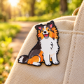 Smiling tricolour collie enamel pin on a canvas bag by a sunlit park path