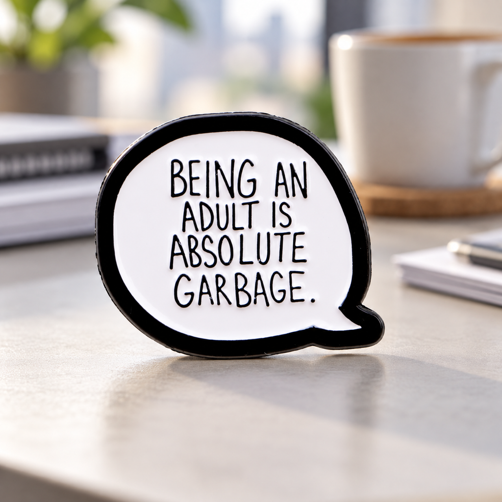 Being an Adult Is Absolute Garbage enamel pin on a desk background