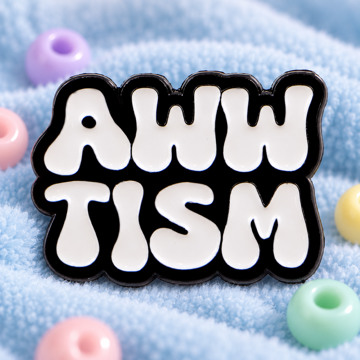 Awwtism enamel pin displayed on soft light-blue sensory fabric with pastel beads