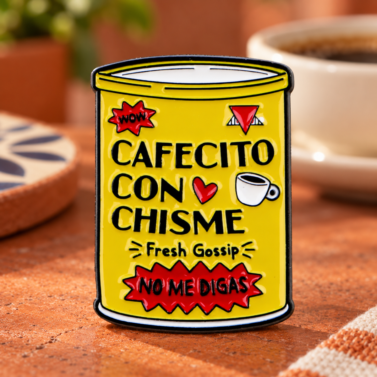 Cafecito Con Chisme enamel pin on a warm café tabletop