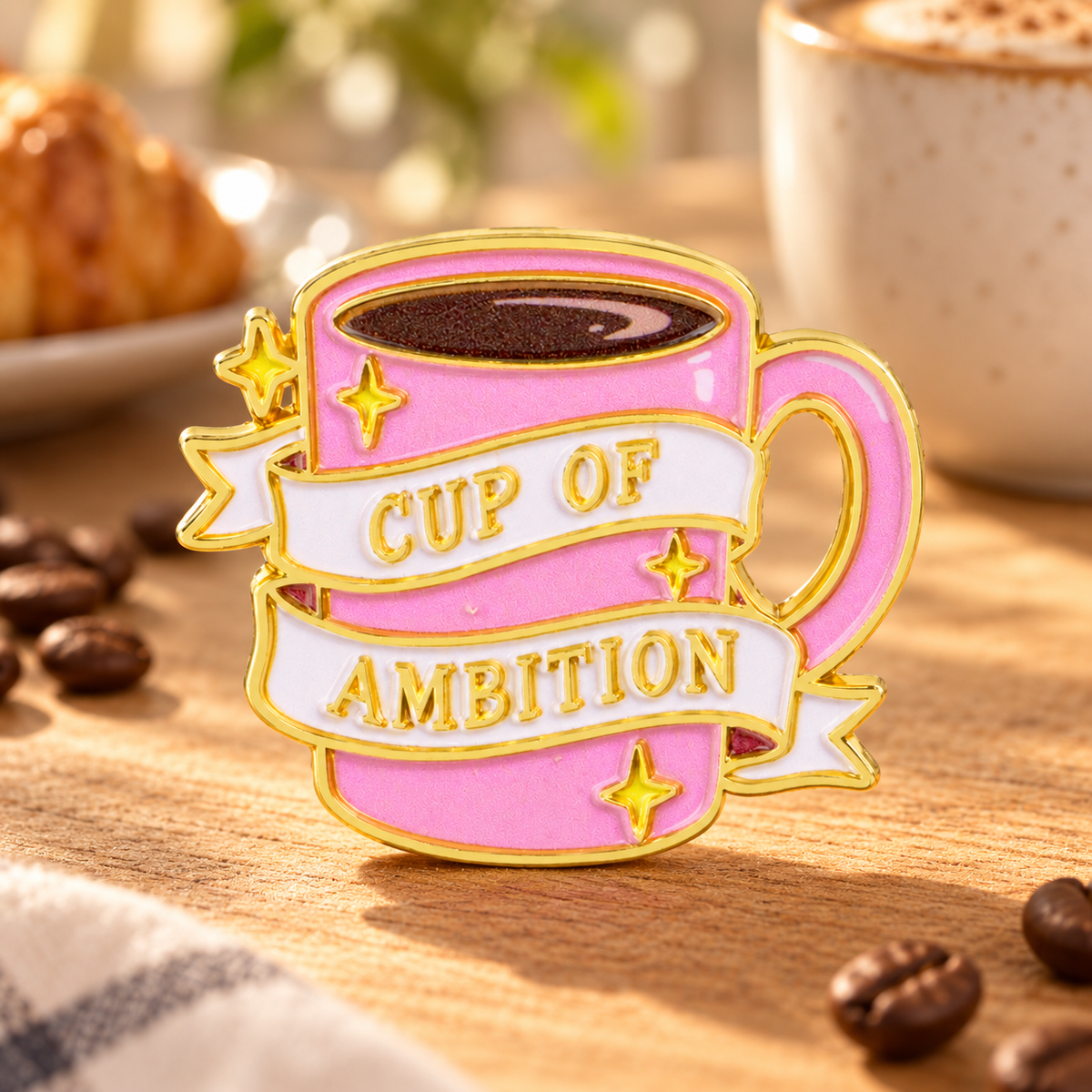 Cup of Ambition pink enamel pin in a sunny cafe