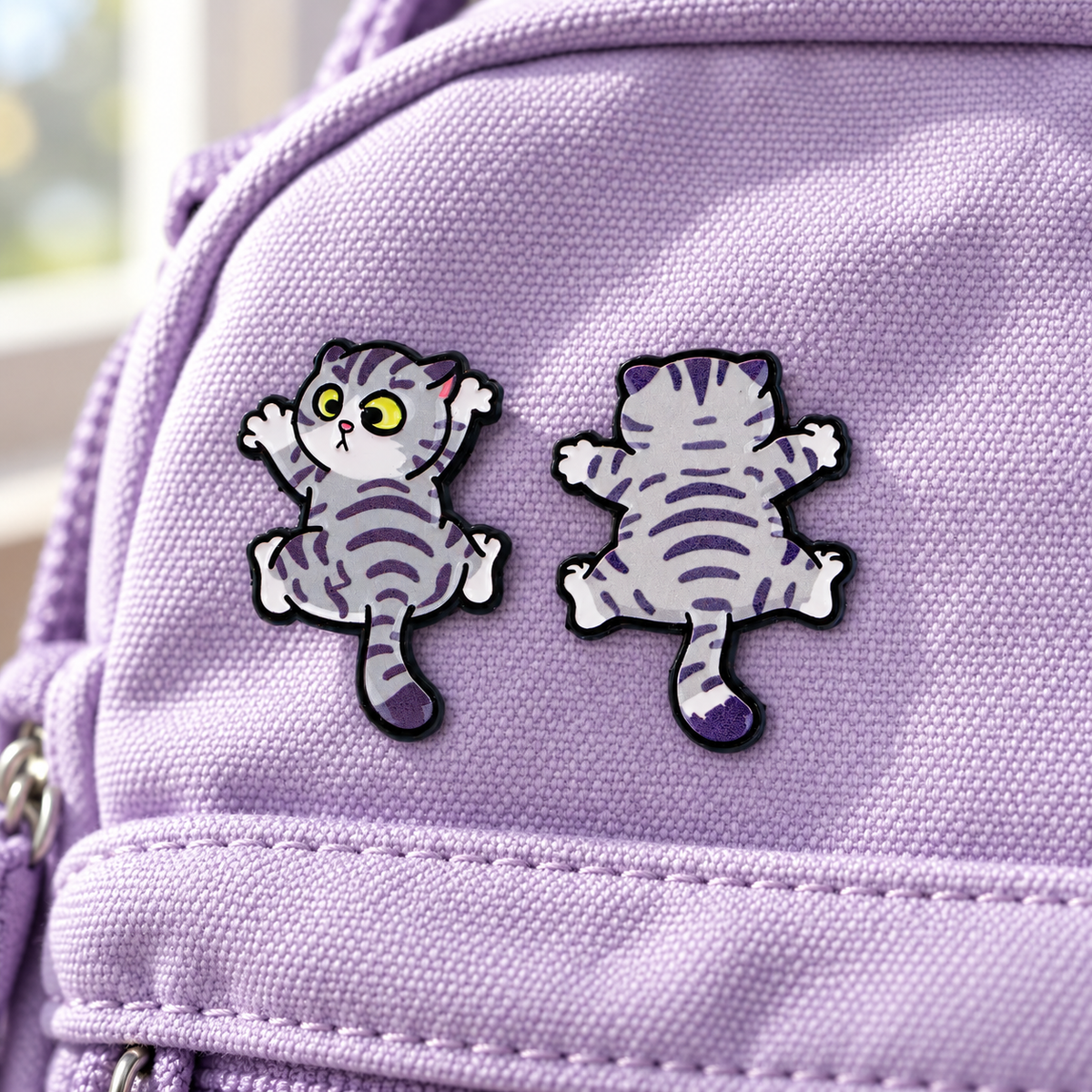Front and back views of a cute grey cat enamel pin on lavender canvas
