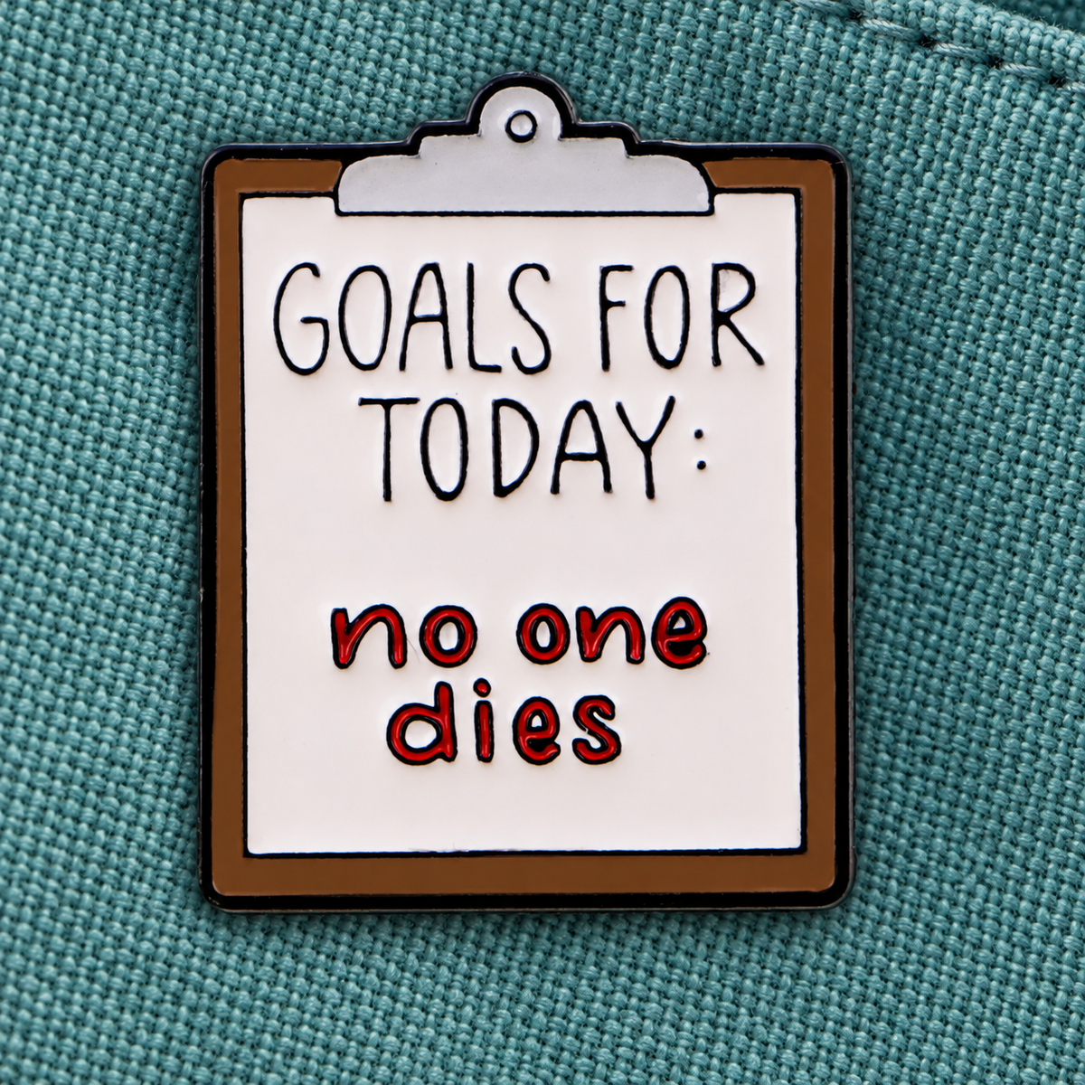 Goals for Today No One Dies enamel pin on teal canvas