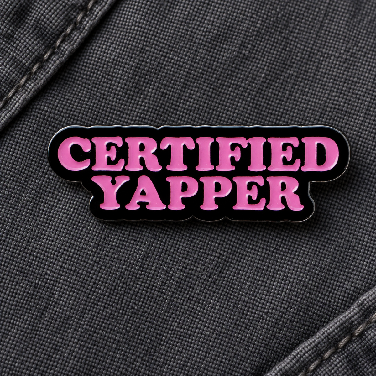 Certified Yapper enamel pin on charcoal fabric