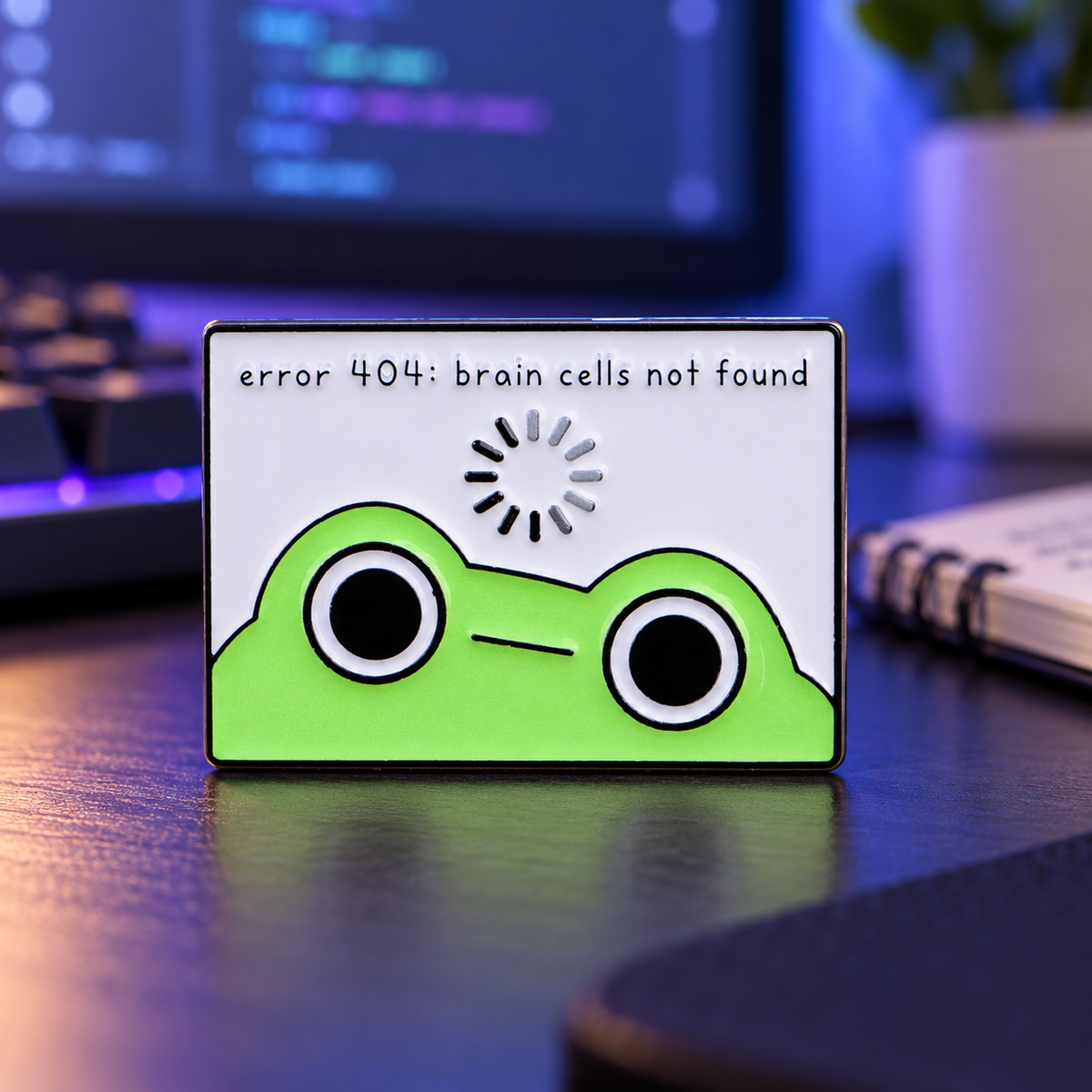 Error 404 Brain Cells Not Found Frog Pin on a softly lit computer desk