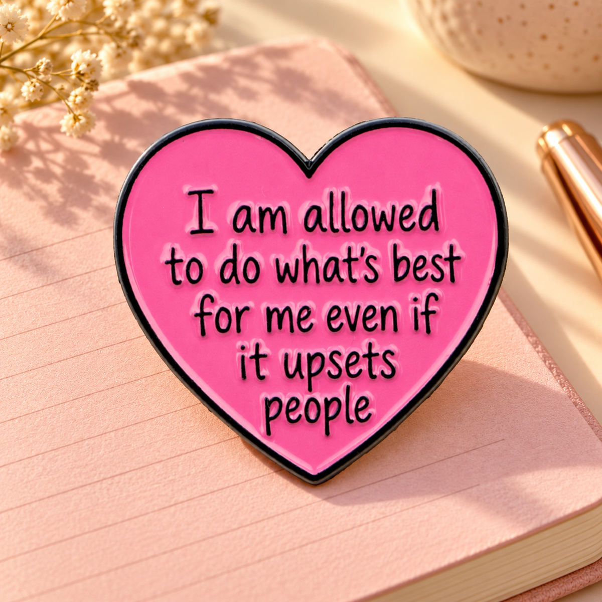 Pink heart enamel pin on a sunlit blush journal