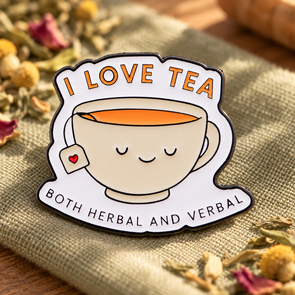I Love Tea Both Herbal and Verbal enamel pin on a cozy herbal tea table