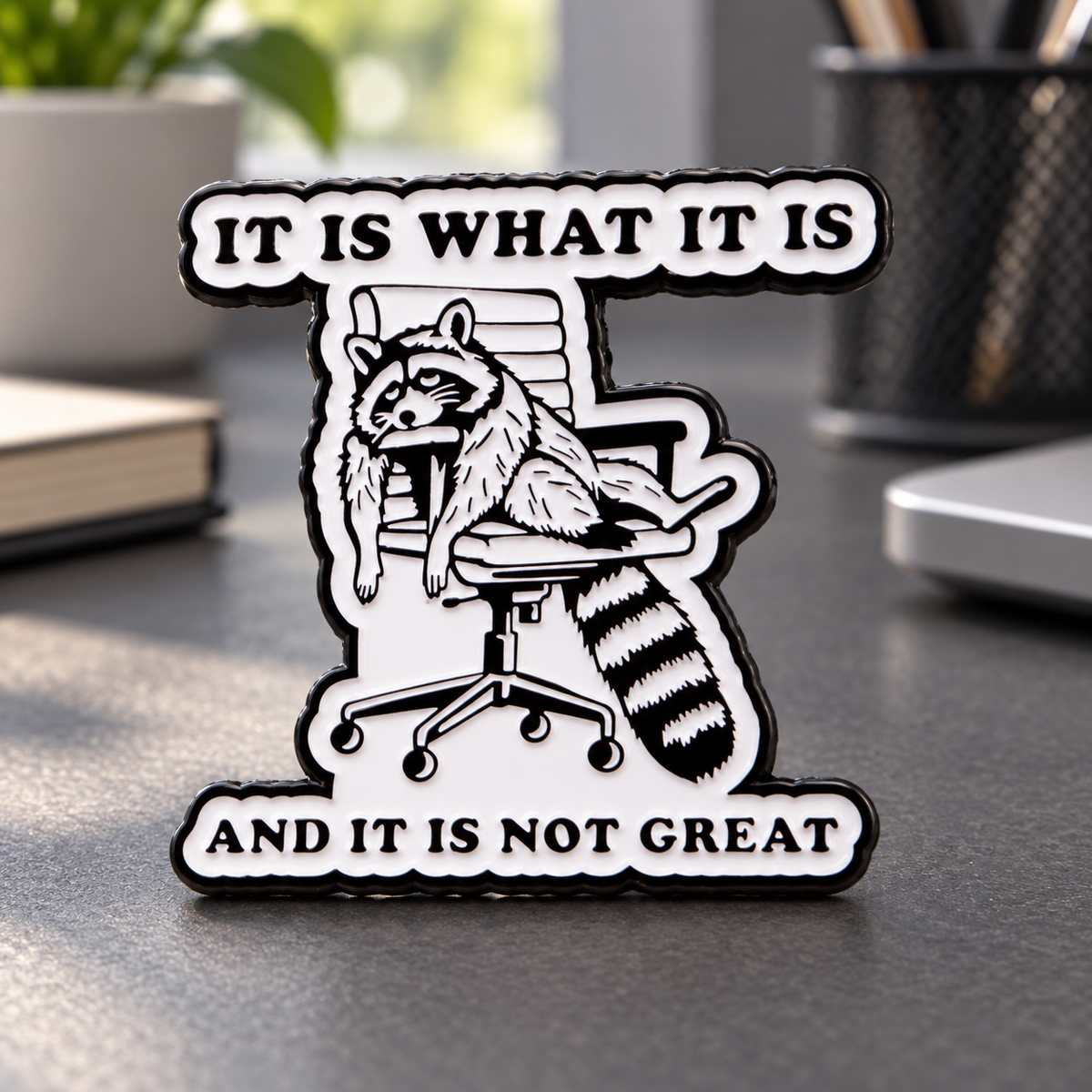 IT IS WHAT IT IS Raccoon Pin on a muted office desk