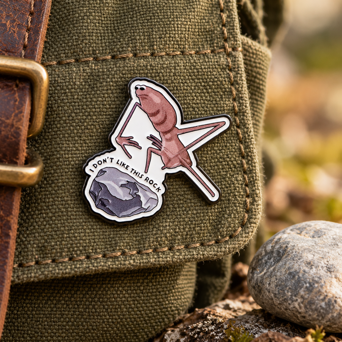 Marcus the Worm enamel pin on a canvas field bag