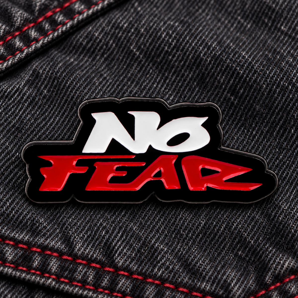 No Fear enamel pin on dark denim with red stitching