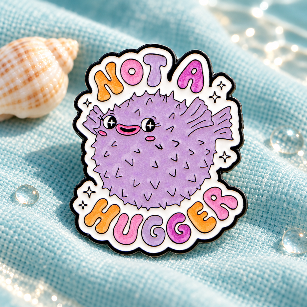 Not A Hugger pufferfish enamel pin displayed on pale aqua fabric with a seashell