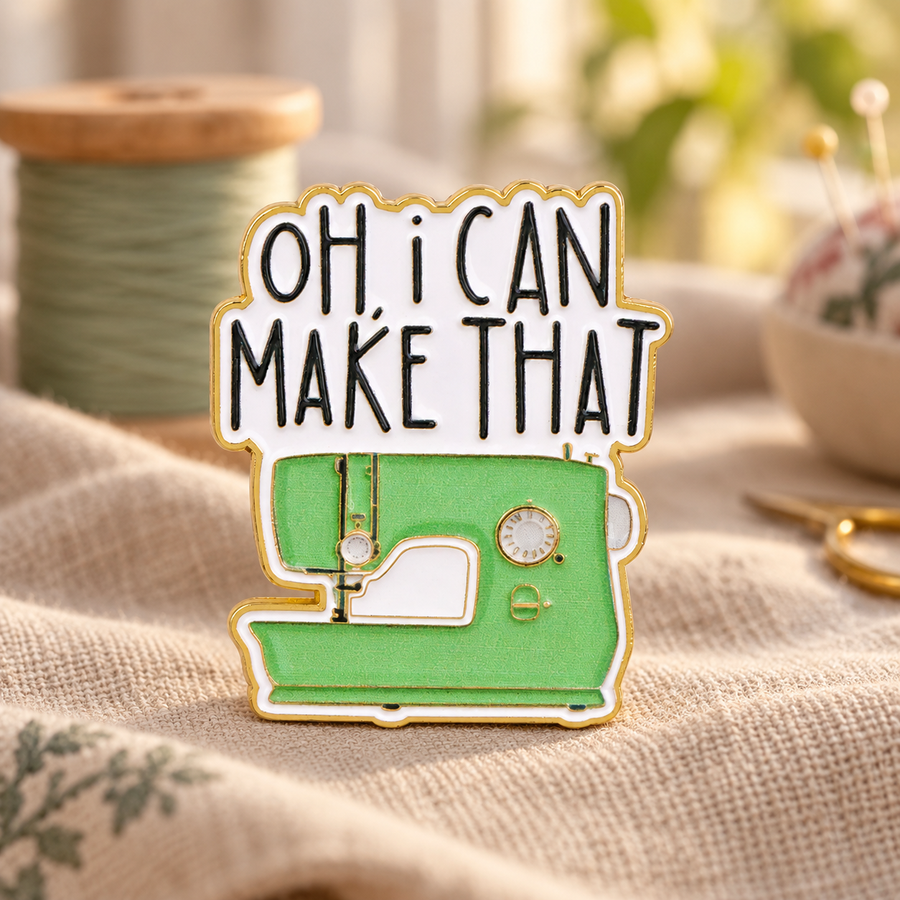 Oh I Can Make That sewing machine enamel pin on a cozy craft table