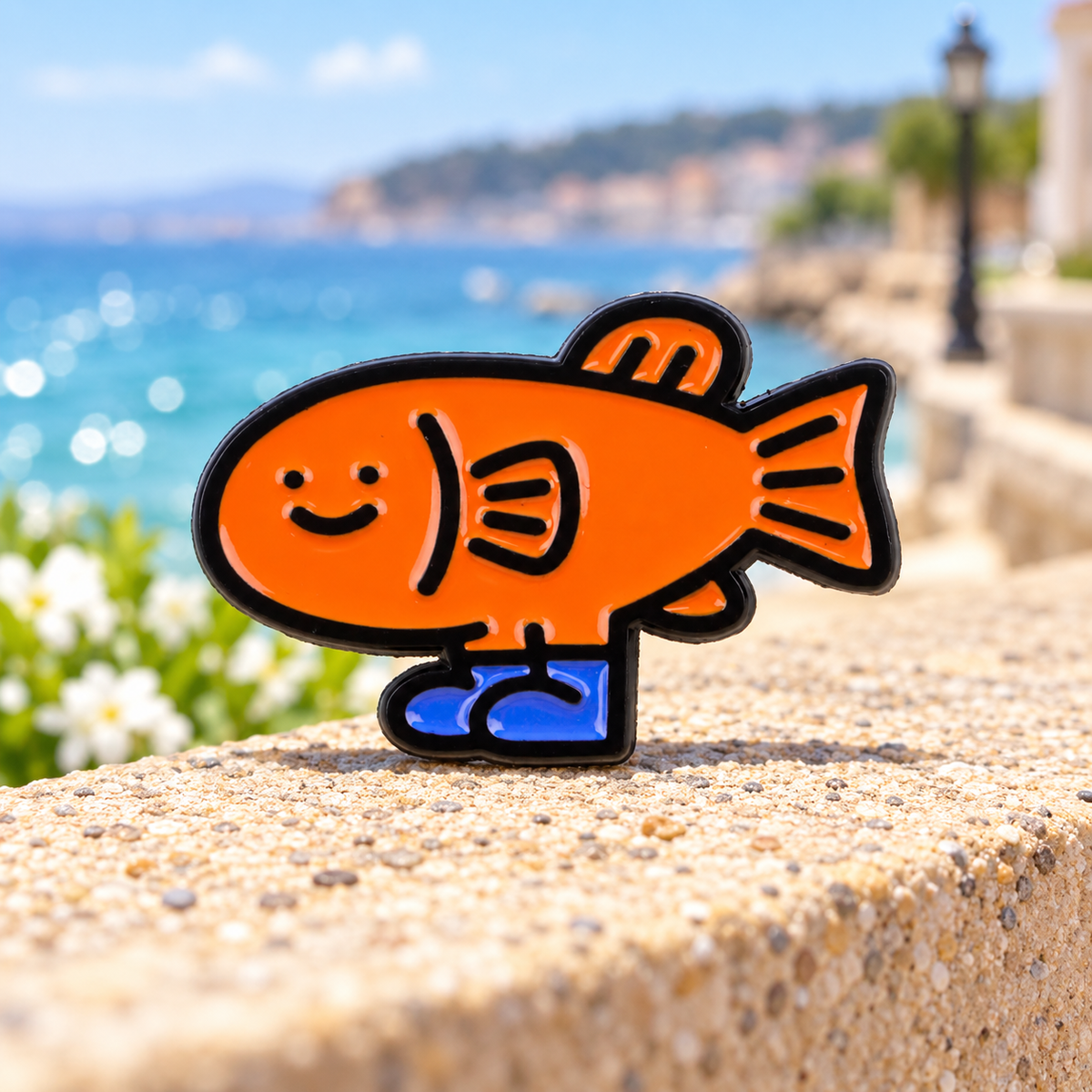 Orange Fish in Blue Shoes enamel pin on a sunny seaside backdrop