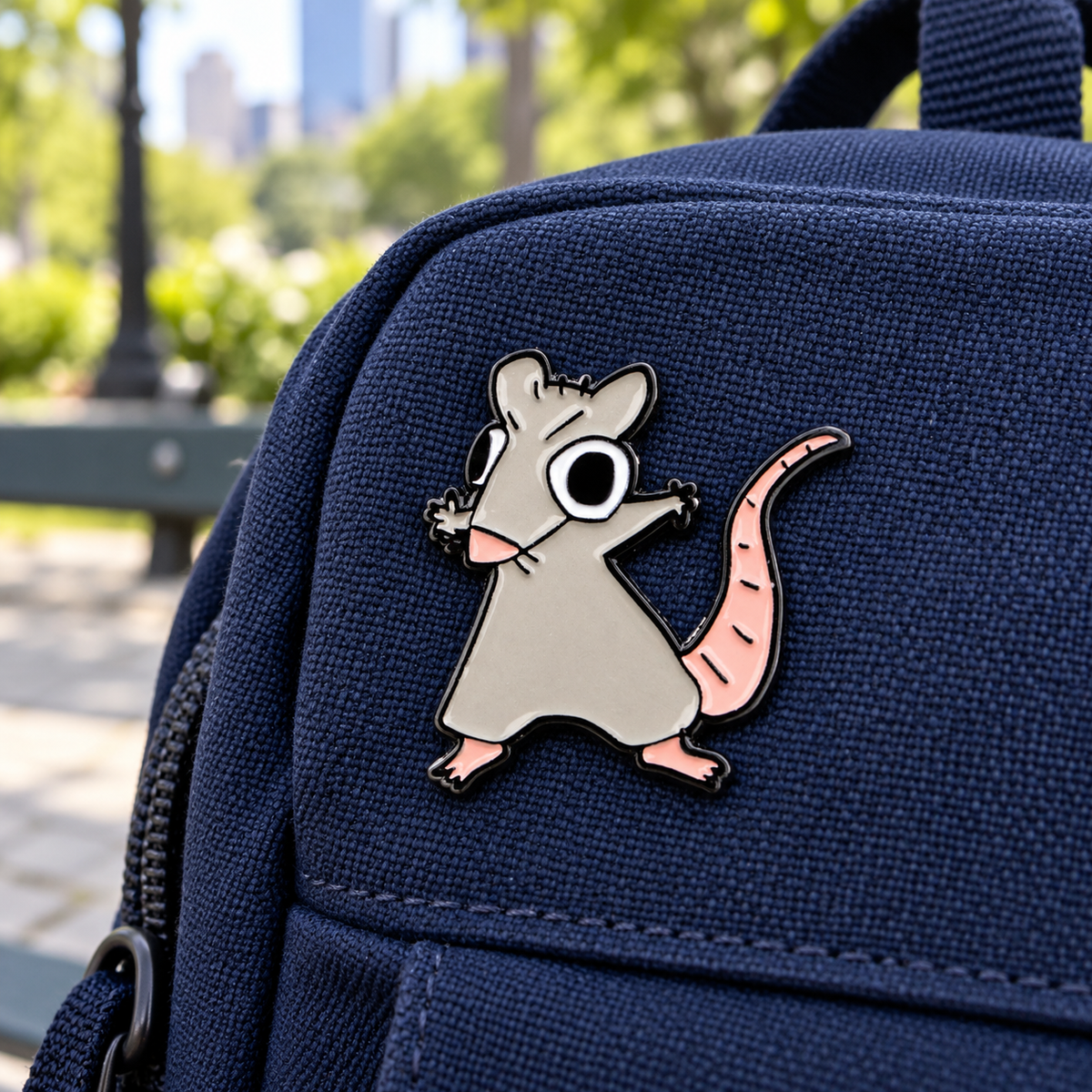 Rat Dance Meme enamel pin on a navy backpack in a city park