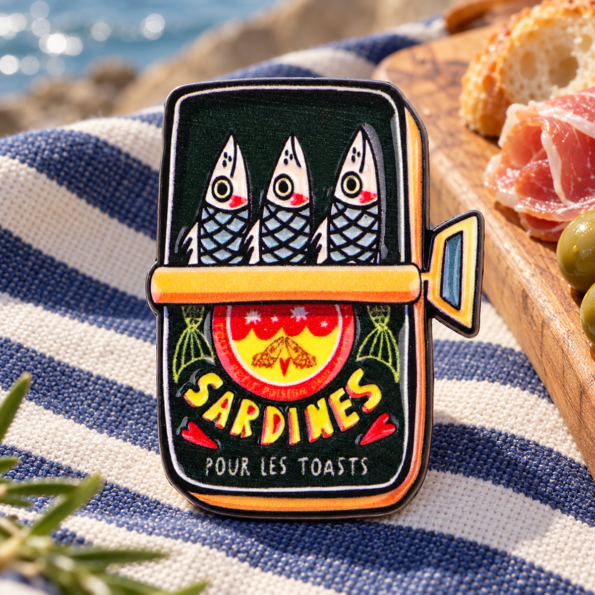 Sardines enamel pin on a striped seaside picnic cloth