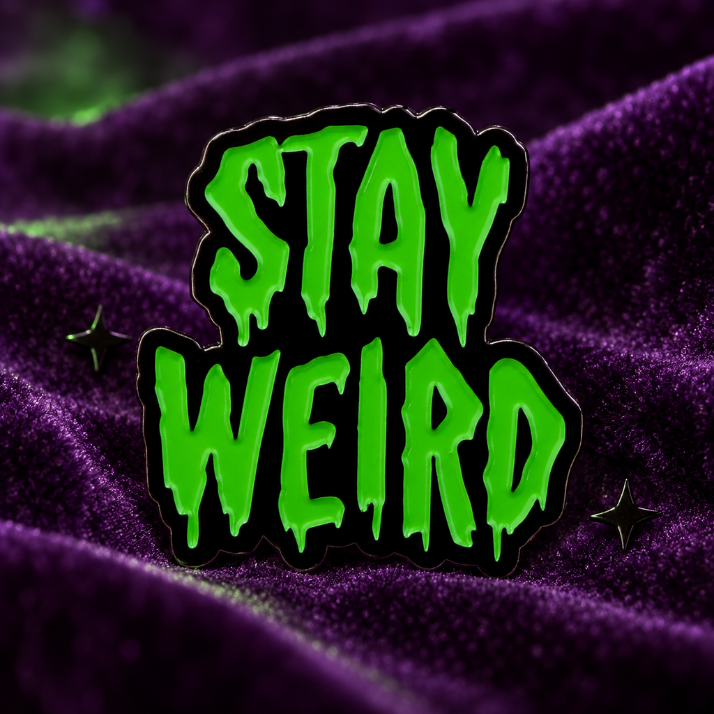 Stay Weird green dripping-letter enamel pin displayed on deep purple velvet