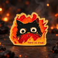 This Is Fine Cat in Flames enamel pin on a dark backdrop with warm ember lights