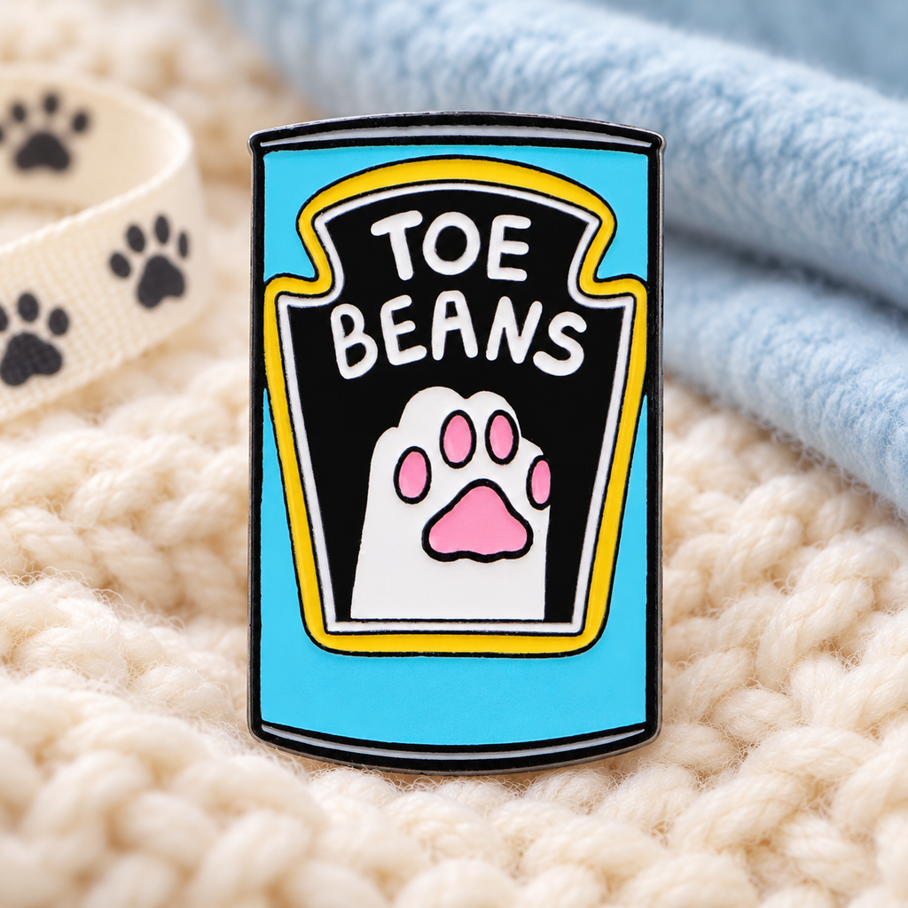 Toe Beans Cat enamel pin on a cozy knitted blanket